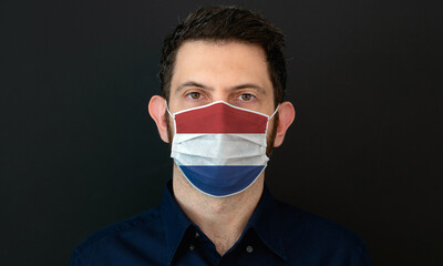 Man wearing Dutch flag protective medical face mask. He looks worried and concerned. Coronavirus concept in Netherlands with black background.
