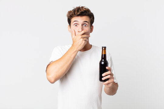 young handsome man covering mouth with hands with a shocked and holding a beer bottle