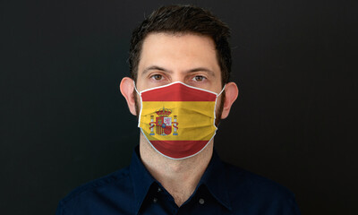 Man wearing Spanish flag protective medical face mask. He looks worried and concerned. Coronavirus concept in Spain with black background.