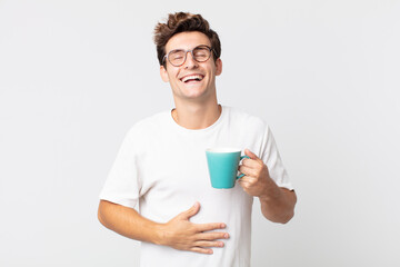 young handsome man laughing out loud at some hilarious joke and holding a coffee cup