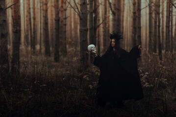 black terrible witch with a skull in the hands of a dead man performs an occult mystical ritual