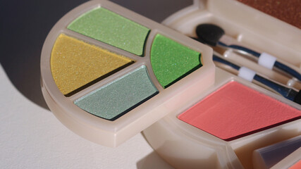 A palette of eye shadow colours on yellow, blue and green hues. Applicator in the background