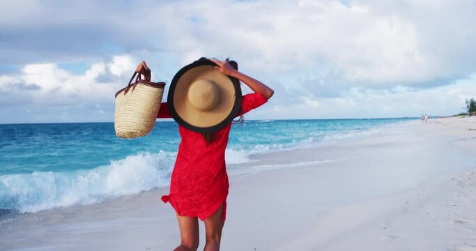 Luxury beach vacation elegant lady running having fun excited, elated, happy, cheering full of joy jumping and dancing on beach holidays with beachwear, sun hat, straw tote bag red and cover-up dress