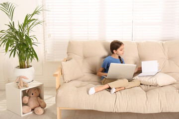 Girl with laptop and book on sofa at home