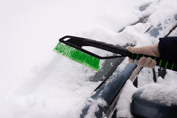 Snow removal, car in snow. Woman cleans the car from snow.