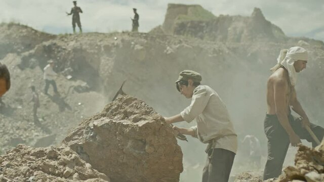 Young miner boy is working in a quarry . Group of many workers are mining with pickaxe in a quarry . Scenic shot in vintage style with artists . Shot on RED EPIC Cinema Camera in slow motion.