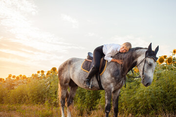 Fototapeta na wymiar woman rides a gray horse in a field at sunset. Freedom, beautiful background, friendship and love for the animal. Sports training equestrian, rental and sale of horses, hiking, riding, walking. Hugs