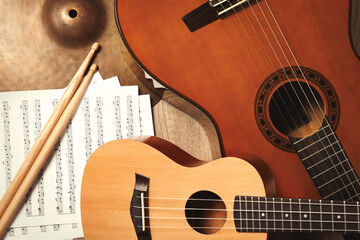 Ukulele, acoustic guitar, drumsticks, cymbal and note sheets on wooden background, flat lay....