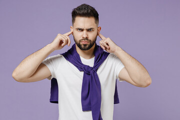 Frowning young brunet man 20s wears white t-shirt purple shirt cover ears with hands fingers do not want to listen isolated pastel violet background studio portrait. People emotions lifestyle concept