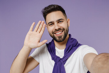 Close up young brunet man 20s wears white t-shirt purple shirt doing selfie shot on mobile phone meet greet waving hand isolated on pastel violet background studio portrait. People emotions concept.