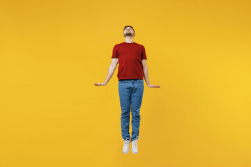 Fototapeta na wymiar Full length cheerful happy young man wear red t-shirt casual clothes jump high clench fists do flying gesture isolated on plain yellow color wall background studio portrait. People lifestyle concept.