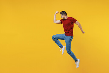 Fototapeta na wymiar Full length profile overjoyed happy young man wear red t-shirt casual clothes jump high clench fists do winner gesture isolated on plain yellow color wall background studio. People lifestyle concept.