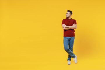 Fototapeta na wymiar Full length smiling happy young man 20s wear red t-shirt casual clothes hold hands crossed folded look aside isolated on plain yellow color wall background studio portrait. People lifestyle concept.