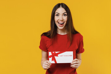 Fototapeta na wymiar Smiling excited fun overjoyed young brunette woman 20s wears basic red t-shirt hold gift certificate coupon voucher card for store keep mouth wide open isolated on yellow background studio portrait