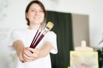 The artist shows the brushes to the camera. Contemporary artist woman. Young entrepreneur, portrait