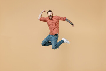 Full size body length excited tatooed young brunet man 20s short haircut wears apricot shirt jump...