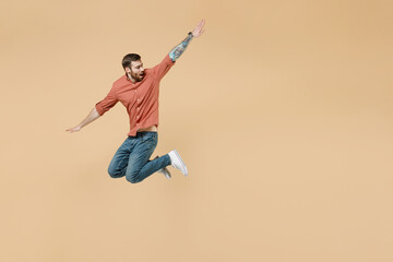 Fototapeta na wymiar Full size body length surprised attractive happy tatooed young brunet man 20s short haircut wears apricot shirt jump like flying look aside back isolated on pastel orange background studio portrait