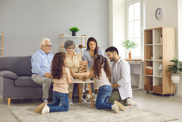 Happy big family gather together in their cozy modern living room. Little sisters playing board...