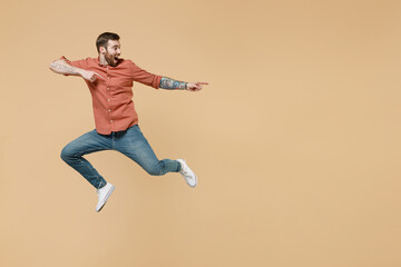 Fototapeta na wymiar Full size body length tatooed young brunet man 20s short haircut wear apricot shirt jump pointing back behind on workspace area copy space mock up isolated on pastel orange background studio portrait