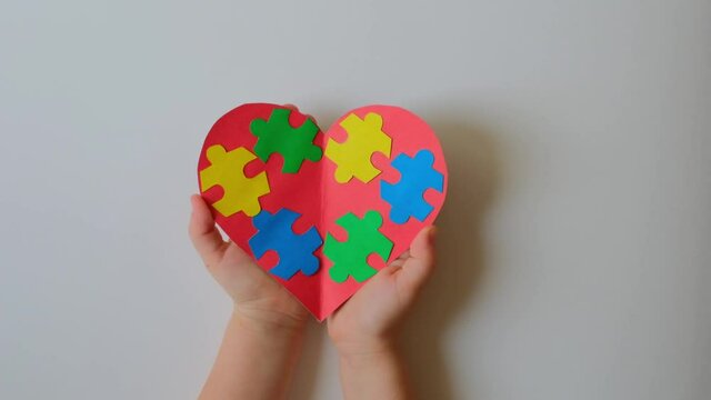 World Autism Awareness Day. Adults and a child hold a heart decorated with colorful puzzle pieces in their hands.  Support for families with autism spectrum disorders. Awareness of autism.