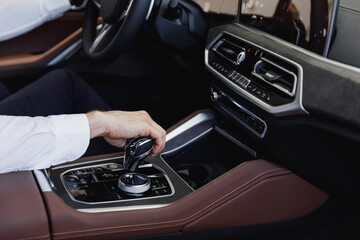 Fototapeta na wymiar Close up cropped up photo shot hands european businessman man wearing white shirt sitting in car salon driving changes gears hold steering wheel automobile modern vehicle. Car sales driver concept