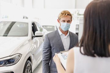Man customer client buyer in classic suit pandemic mask choose auto want buy new car automobile consult with salesman read papers in showroom salon dealership store motor show indoor Sale concept.