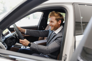 Side view man happy customer male buyer client in classic grey suit driving car hold wheel choose auto want buy new automobile in showroom vehicle salon dealership store motor show indoor Sale concept