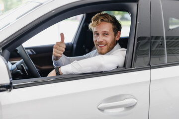 Smiling man customer male buyer client in white shirt drive car hold wheel show thumb up choose...