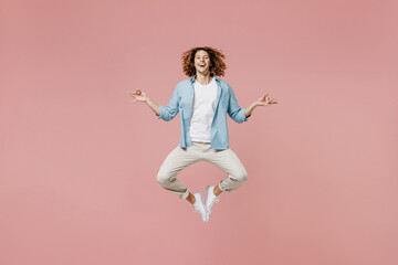 Full length young man 20s with long curly hair in casual clothes hold spread hand in yoga om aum gesture relax meditate try to calm down jump high isolated on pastel plain pink wall background studio