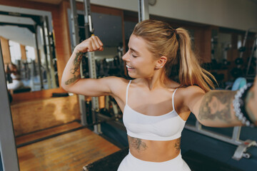 Close up young strong athletic sportswoman woman in white sportswear warm up training sit near treadmill trainers do selfie shot on mobile cell phone show muscles in gym indoors Workout sport concept - obrazy, fototapety, plakaty