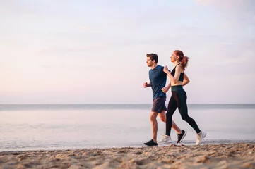 Outdoor-Kissen Full body side view couple young two friends strong sporty sportswoman sportsman woman man in sport clothes warm up training run on sand sea ocean beach outdoor jog on seaside in summer day morning. © ViDi Studio