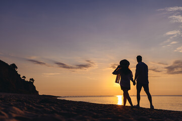 Full size back view silhouette young couple two friends family man woman in casual clothes hold hands walk stroll together at sunrise over sea beach ocean outdoor exotic seaside in summer day evening.