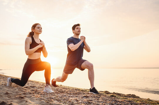 Full body sunlit couple young two friend sporty sportswoman sportsman woman man 20s in sport clothes warm up training do lunges do exercise on sea ocean beach outdoor on seaside in summer day morning.
