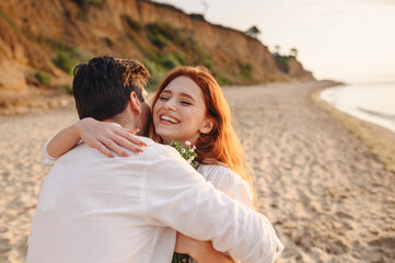 Excited young lovely couple two family man woman in white clothes hug each other hold flowers enjoy together at sunrise over sea ocean sand beach outdoor exotic seaside in summer day sunset evening.