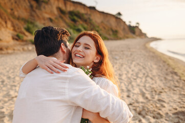 Fototapeta premium Excited young lovely couple two family man woman in white clothes hug each other hold flowers enjoy together at sunrise over sea ocean sand beach outdoor exotic seaside in summer day sunset evening.