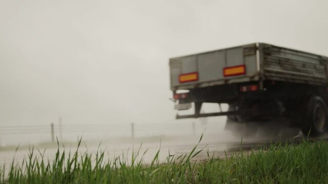 A red flatbed semitrailer tractor driving on the road in rain and poor visibility in summer. Poor visibility concept in bad weather, logistic. Slow motion