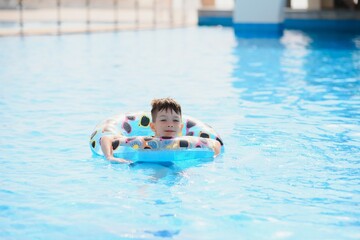 Naklejka premium Happy boy in swimming pool. Boy is alone, swimming inflatable ring and surronded by water splashes. Wet teenager is enjoying summer weekend in amusement water park. Banner with copy space
