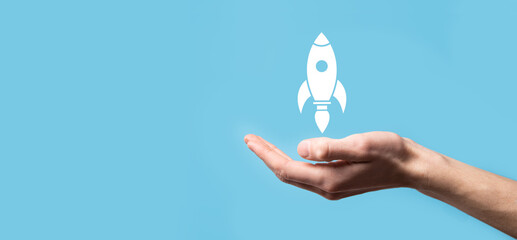 Male hand holding rocket icon that takes off, launch on blue background. rocket is launching and...