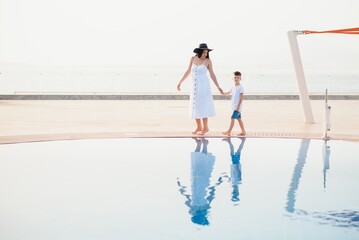 Young mother and son walking near swimming pool. Summer vacation concept