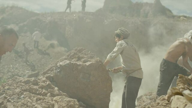 Young miner boy is working in a quarry . Group of many workers are mining with pickaxe in a quarry . Scenic shot in vintage style with artists . Shot on RED EPIC Cinema Camera in slow motion.