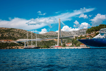 Fototapeta na wymiar Port in Dubrovnik, Croatia. Summer landscape with road, bridge, boat, harbor, city, mountains, blue sea. Luxury cruise. View from the water to the floating liner