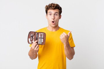young handsome man looking astonished in disbelief and holding a nails tools case