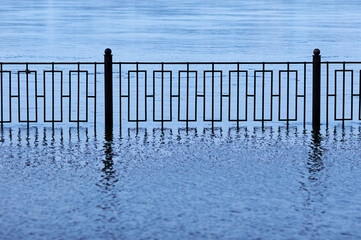 A metal fence of a flooded embankment with reflections. Selective focus on the geometric grid.