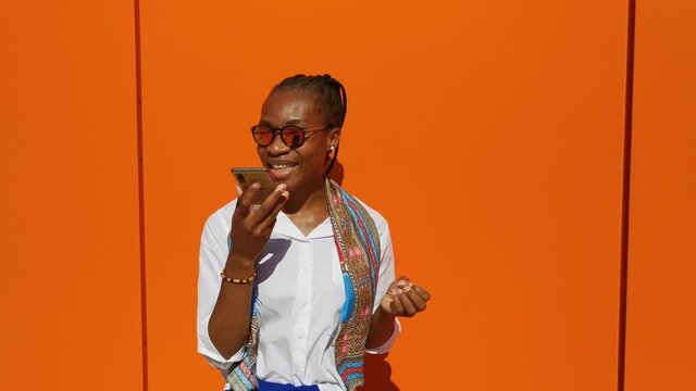 Video de empresaria africana con gafas de sol, mandando un audio en fondo naranja.