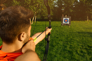 Man with bow and arrow aiming at archery target in park, back view - obrazy, fototapety, plakaty