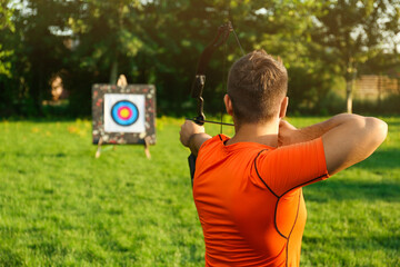 Man with bow and arrow aiming at archery target in park, back view