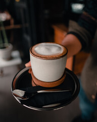 Hand holding a mug of cappuccino. Barista surving in coffee shop.