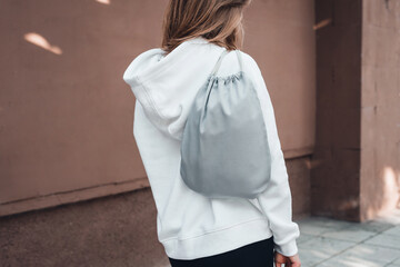 Grey drawstring pack template, mockup of bag for sport shoes on woman's shoulder.