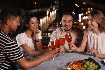 Friends with glasses of cocktails spending time together on roof cafe terrace at night