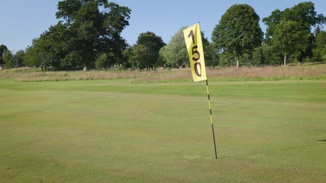 150 yard flag on a golf driving range. Sunny day with blue sky and well cut green grass with trees in the background.
